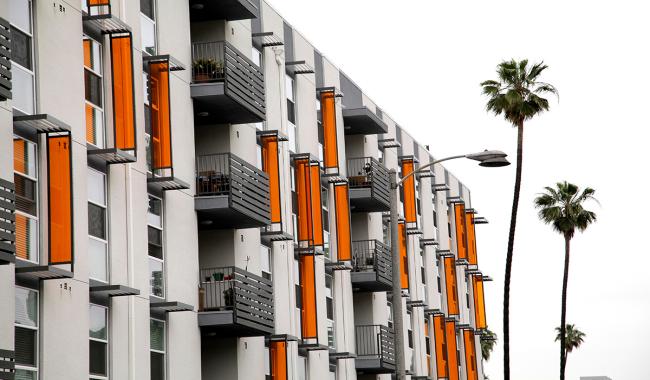 A facade of a multi-family housing apartment building accompanied with palm trees in the background