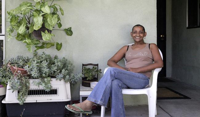 A woman sitting at the front patio of an apartment unit with green potted plants in the background