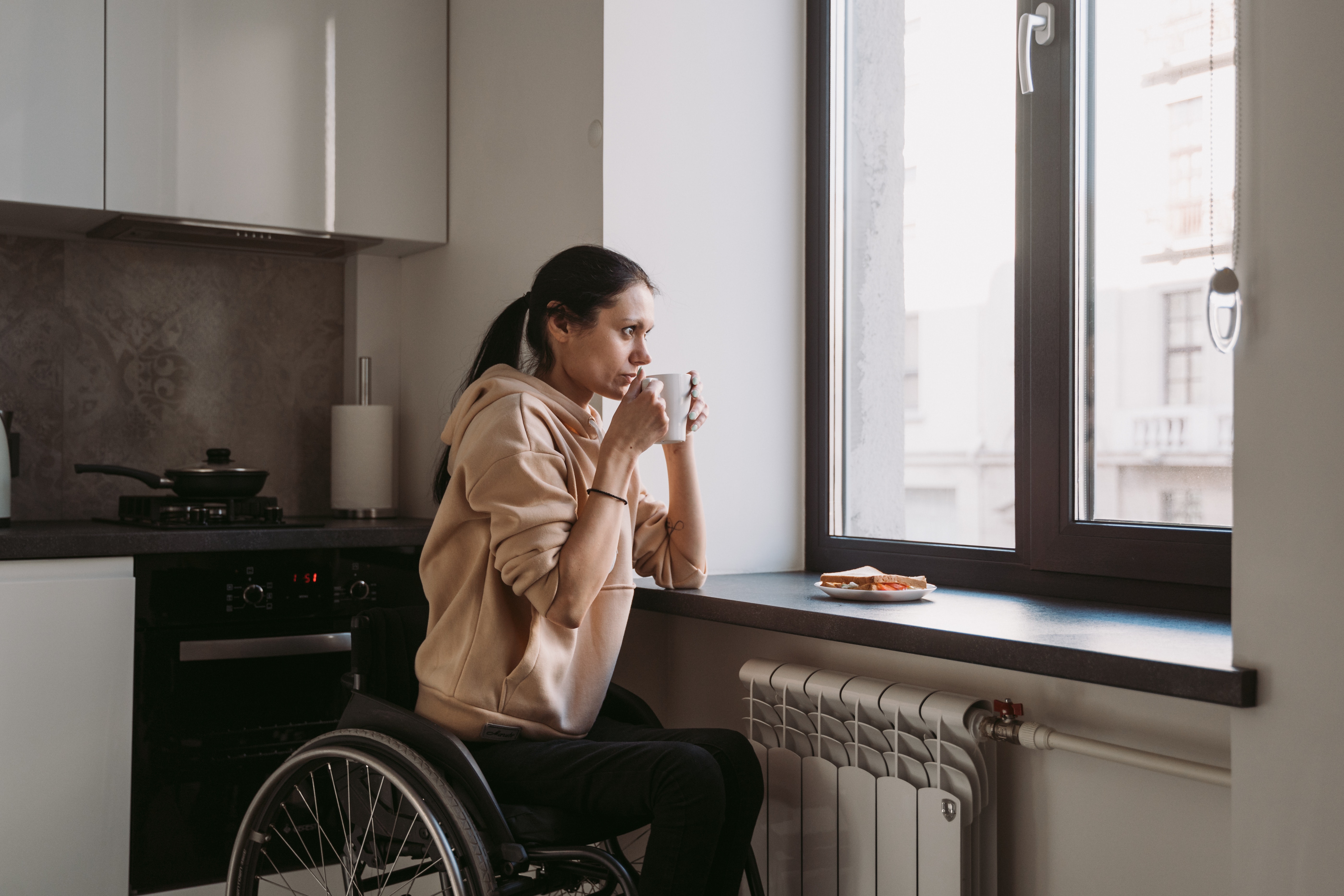 lady in wheelchair sipping on coffee & looking outside the window